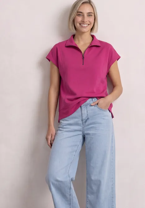 Mouwloos shirt met Silk-Look en ritssluiting magenta dream Eine lächelnde Frau trägt ein pinkes Polo-Shirt mit Reißverschluss und helle, weite Jeans.