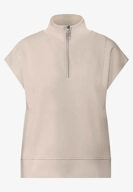 Beiges Top mit kurzen Ärmeln, Stehkragen und kurzem Reißverschluss, minimalistischer Stil.
