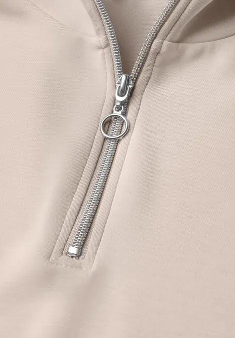 Beiger Kapuzenpullover mit halbem Reißverschluss und rundem Zipper-Anhänger.