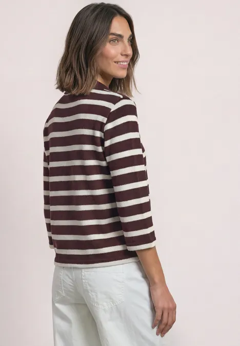 Frau in weißer Hose und bordeaux-weiß gestreiftem Shirt blickt lächelnd über die Schulter.