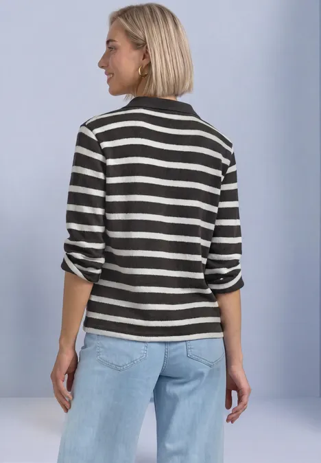 Polo met 3/4-mouwen en streepjespatroon black coffee Vrouw van achteren in zwart-wit gestreept shirt en lichtblauwe spijkerbroek voor een lichte achtergrond.