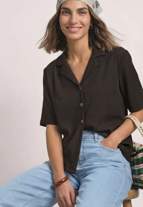 Shirt met verschillende texturen en een knoopsluiting black coffee Vrouw glimlacht in een bruin kort shirt, lichte hoofddoek en jeans, met een gevlochten tas.