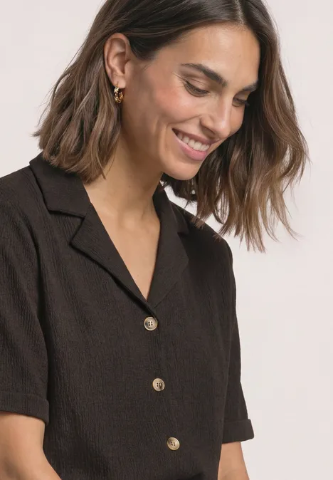 Shirt met verschillende texturen en een knoopsluiting black coffee Vrouw met halflang bruin haar lacht, draagt een donkerbruine blouse met gouden knopen.