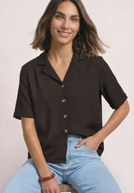 Shirt met verschillende texturen en een knoopsluiting black coffee Vrouw in een bruin kortmouwig blouse met knopen en lichtblauwe jeans, glimlachend met hand in zak.