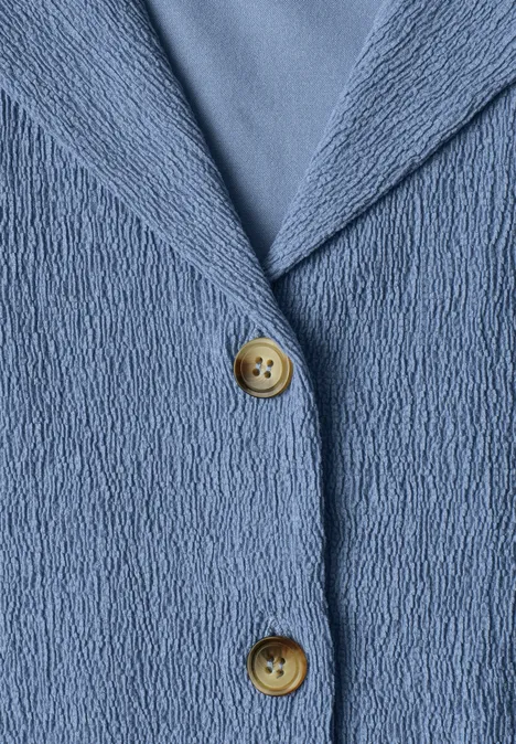Makroaufnahme einer blau strukturierten Jacke mit zwei runden Holzknöpfen.
