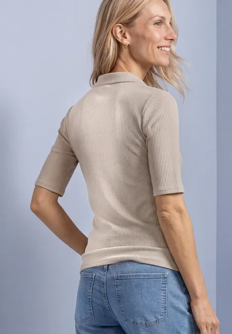 Poloshirt im Strick-Look mit Rippstruktur clay sand mel. Frau von hinten in beigem Kurzarm-Pullover und Jeans, seitlich lächelnd vor hellem Hintergrund.