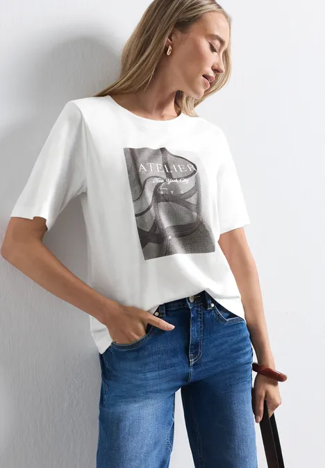 Shirt met ronde hals en fotoprint off white Frau in weißem T-Shirt mit Fotoprint, blauen Jeans und Tasche, vor einer weißen Wand posierend.