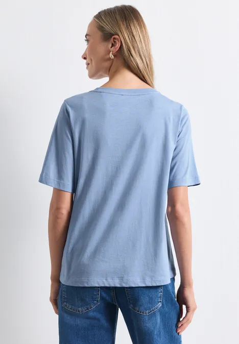 Shirt met ronde hals en fotoprint northern blue Eine Frau steht mit dem Rücken zur Kamera, sie trägt ein hellblaues T-Shirt und Jeans.