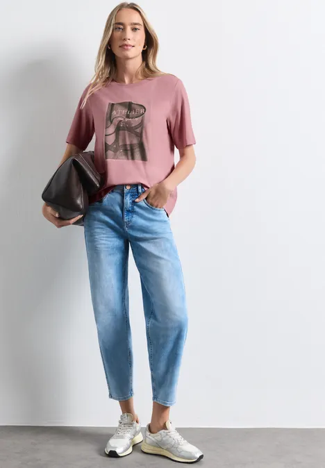 Shirt met ronde hals en fotoprint vintage blush Frau trägt rosa T-Shirt mit Print, helle Jeans, Sneaker und hält eine schwarze Tasche.