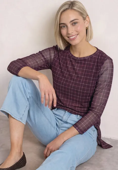 Shirt met 3/4-mouwen van mesh met print rustic rouge Eine lächelnde Frau in kariertem Pullover und Jeans sitzt entspannt auf dem Boden.