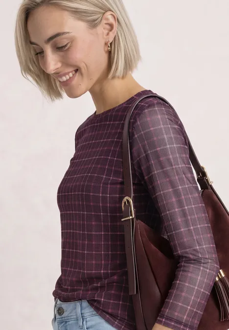 Shirt met 3/4-mouwen van mesh met print rustic rouge Lächelnde blonde Frau in kariertem violetten Oberteil mit Schultertasche vor hellem Hintergrund.