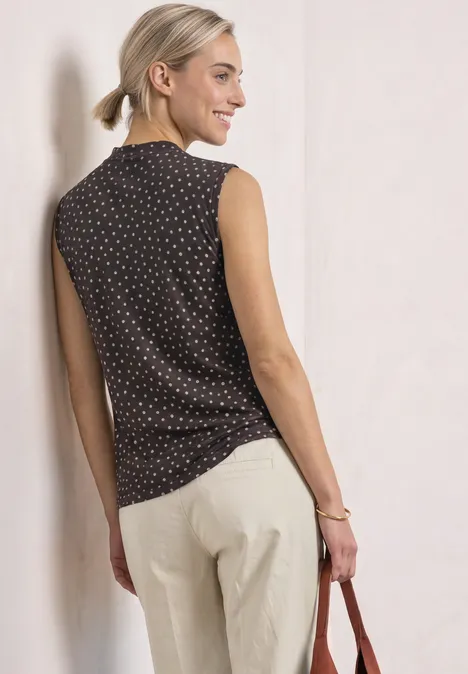 Turtleneck-top van mesh met print black coffee Vrouw draagt een mouwloze, zwarte polkadot top met lichte broek, houdt een tas vast en glimlacht zijwaarts.
