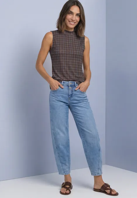 Turtleneck-top van mesh met print silk brown Vrouw lacht voor een lichte achtergrond, draagt een geruit mouwloos topje, wijde jeans en bruine sandalen.