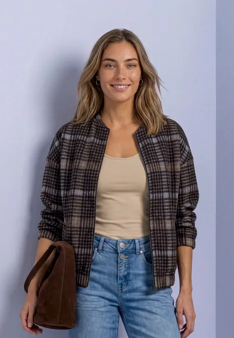 Eine Frau lächelt, trägt kariertes Jackett, beiges Top und Jeans.