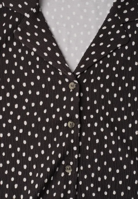 Shirt met verschillende texturen en een knoopsluiting black coffee Zwarte blouse met witte stippen en V-hals, voorzien van drie knopen op lichte achtergrond.