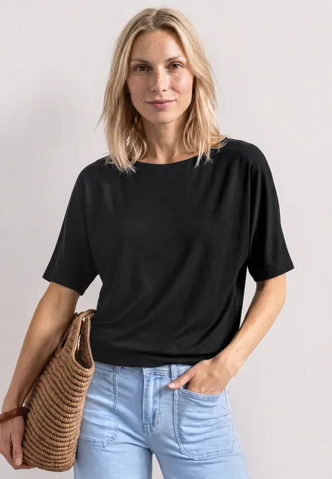 Eine Frau mit schwarzem T-Shirt, hellblauen Jeans und einem Korb-Strohtasche.