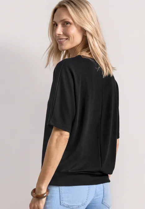 Frau steht mit dem Rücken zur Kamera, trägt schwarzes T-Shirt und blaue Jeans.