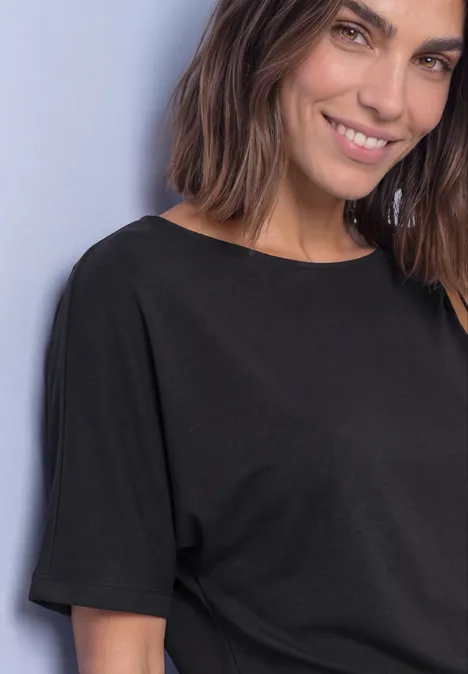 Femme aux cheveux bruns mi-longs, souriante en haut noir devant un fond clair.