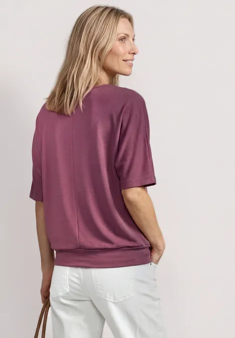 Frau von hinten in rosa T-Shirt, weißen Jeans und Handtasche.
