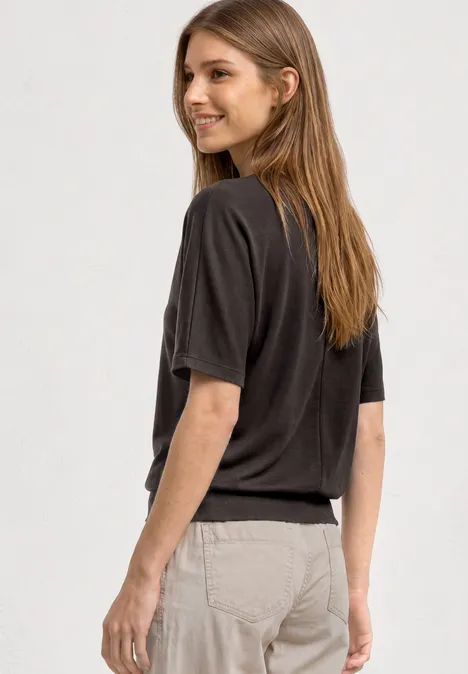 Seitliche Aufnahme einer Person mit dunkelgrauem Shirt und hellen Hosen vor weißem Hintergrund