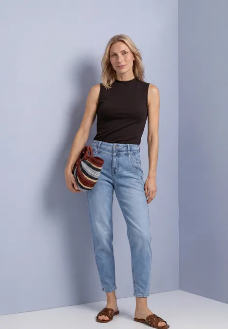 Top in Silk-Look met coltrui black coffee Frau mit schwarzem Top und hellblauen Jeans, trägt gestreifte Tasche und braune Sandalen.