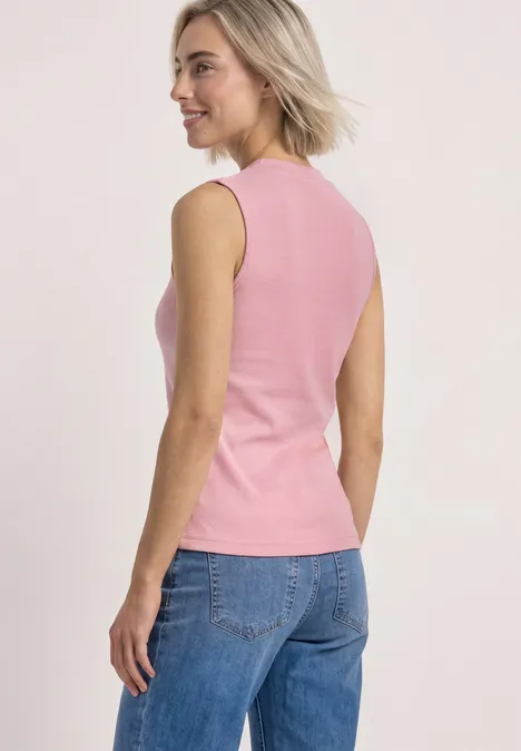 Frau mit kurzem blondem Haar trägt ein rosa ärmelloses Top und blaue Jeans, von hinten gezeigt.