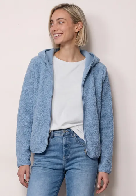 Blonde Frau in lässiger Alltagskleidung mit Jeans, T-Shirt und blauer Fleecejacke, lächelnd