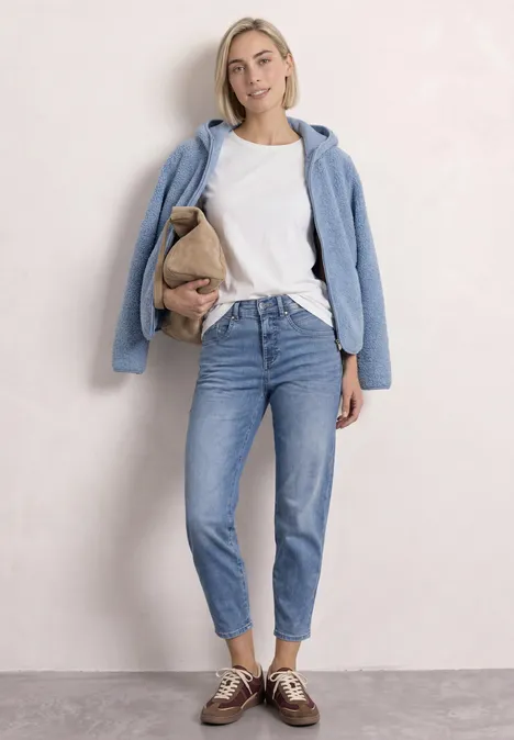 Junge Frau in weißem T-Shirt, Jeans und blauer Jacke trägt eine Tasche.