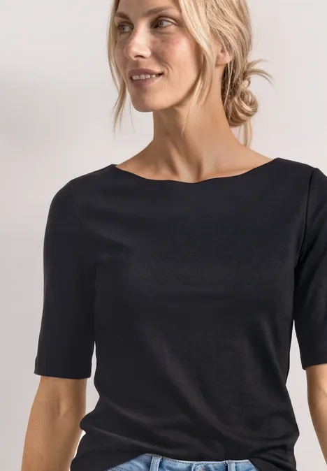 Nahaufnahme einer lächelnden Frau mit zurückgebundenem blonden Haar, die ein schwarzes Shirt trägt.