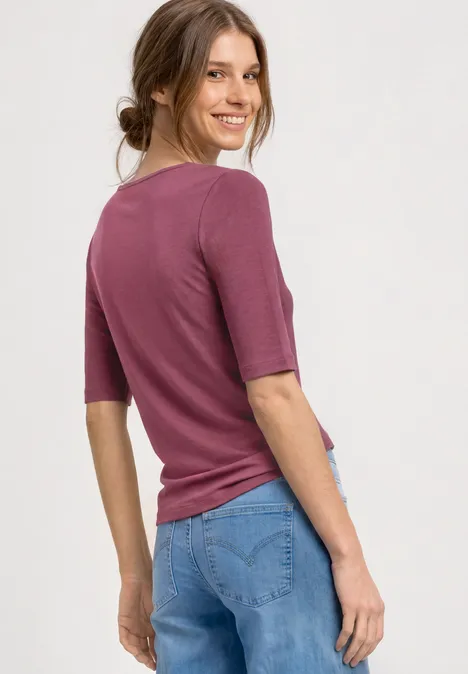 Frau mit lila Shirt und blauen Jeans, Rückenansicht vor hellem Hintergrund.
