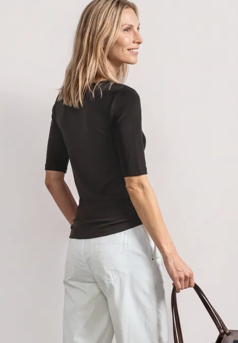 Frau von hinten in schwarzem Oberteil und weißer Hose, hält eine braune Tasche.