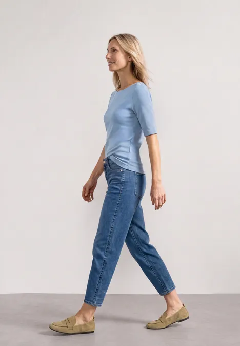 Frau in blauem Shirt und Jeans läuft seitlich vor hellem Hintergrund.