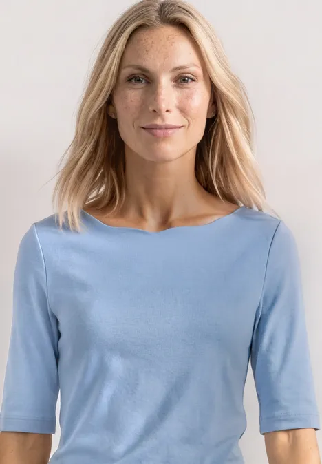 Frau in hellblauem Halbarmshirt vor neutralem Hintergrund