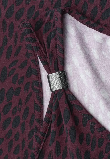Top mit V-Neck und Dekodetail rustic rouge Ein dunkelroter Vorhang mit schwarzem Tupfenmuster, von einer silbernen Klammer zu eleganter Schleife gebunden.