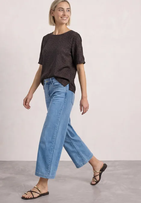 T-Shirt mit Rundhals und Strukturmix molten earth Frau mit schwarzem T-Shirt und weitem Jeans läuft lächelnd.
