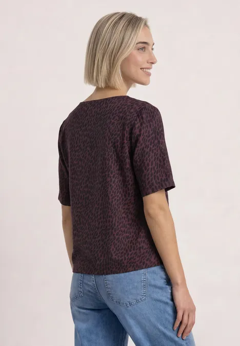 T-shirt à col rond et mélange de textures rustic rouge Frau mit kurzem blondem Haar in lila T-Shirt mit kleinem Muster und blauen Jeans, im Profil stehend.
