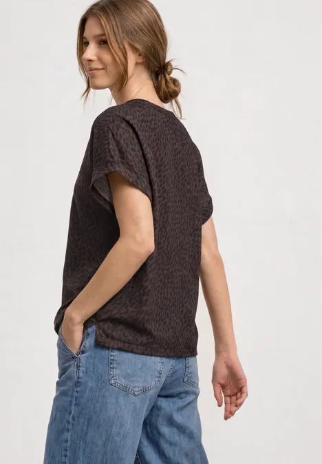 Frau in schwarzem T-Shirt mit Muster und blauer Jeans, seitlich im Profil, mit locker zusammengebundenem Haar.