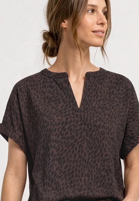 Frau trägt dunkles, kurzärmeliges Oberteil mit dezentem Animal-Print und V-Ausschnitt.