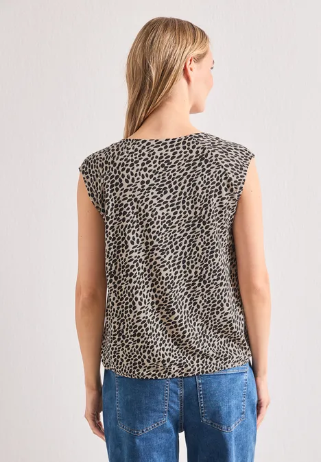 Shirt mit Boat Neck und Elastikbund cotton beige Frau von hinten in ärmellosem, gepunktetem Top und blauen Jeans vor hellem Hintergrund.
