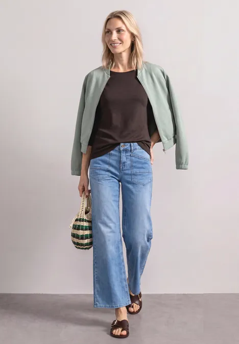 Shirt met 3/4-mouwen en een boothals black coffee Vrouw in losse jeans, zwart topje en groen jasje, met rieten tas en sandalen voor neutrale achtergrond.