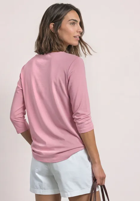 Frau von hinten in rosa Langarmshirt und weißen Shorts, hält eine Tasche und blickt seitlich.