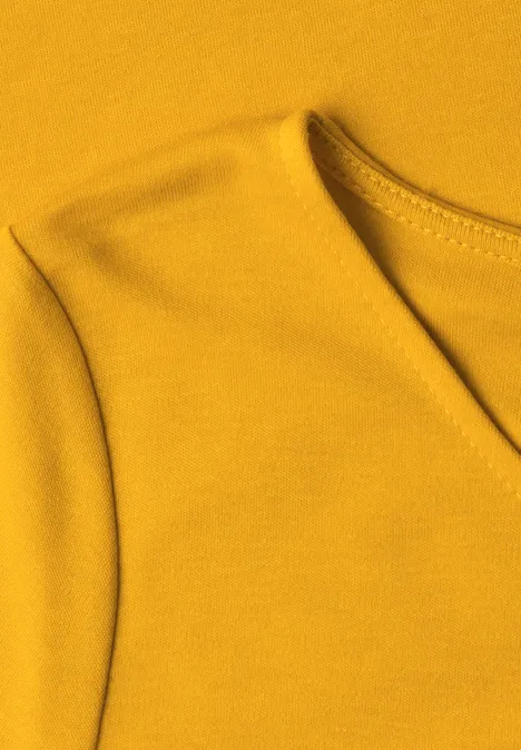 Naheaufnahme eines senfgelben T-Shirts aus Baumwolljersey mit V-Ausschnitt und Schulternaht.