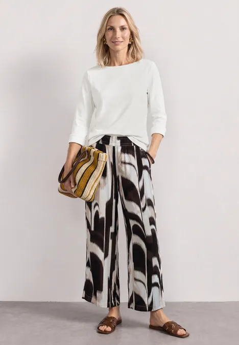 3/4-Arm Shirt mit U-Boot-Ausschnitt off white Frau in weißem 3/4-Shirt und weiter schwarz-weiß gemusterter Hose, mit gestreifter Tasche und Sandalen.