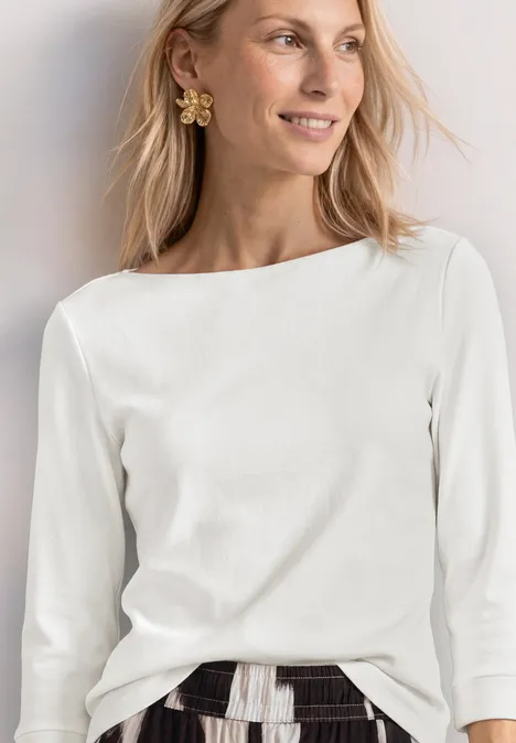 3/4-Arm Shirt mit U-Boot-Ausschnitt off white Frau trägt weiße 3/4-Ärmel-Bluse mit U-Boot-Ausschnitt, gemusterten Rock und Blumenohrring.