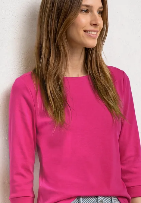 Frau mit pinkem Langarmshirt vor hellem Hintergrund