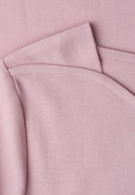 Nahaufnahme von rosa Baumwollstoff mit sichtbaren Nähten, vermutlich Teil eines T-Shirts oder Babykleidung.