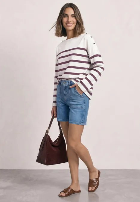 Frau in gestreiftem Pullover, Jeans-Shorts, braunen Sandalen mit passender Tasche vor hellem Hintergrund.