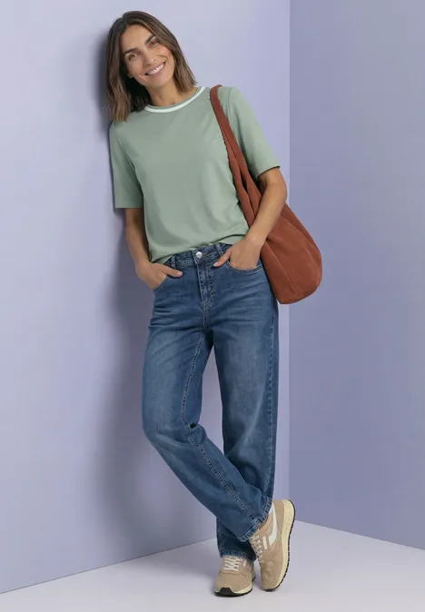 Shirt met ronde hals en contrasterende details eucalyptus green Frau in hellgrünem T-Shirt mit weißem Kragen, Jeans und brauner Umhängetasche lehnt lächelnd an lila Wand.