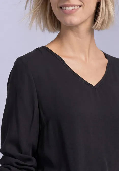 Fröhliche Frau mit kurzen blonden Haaren trägt ein schwarzes V-Ausschnitt-Shirt.