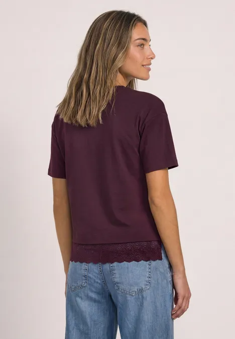 Eine Frau steht mit dem Rücken zur Kamera, trägt ein violettes T-Shirt und blaue Jeans.